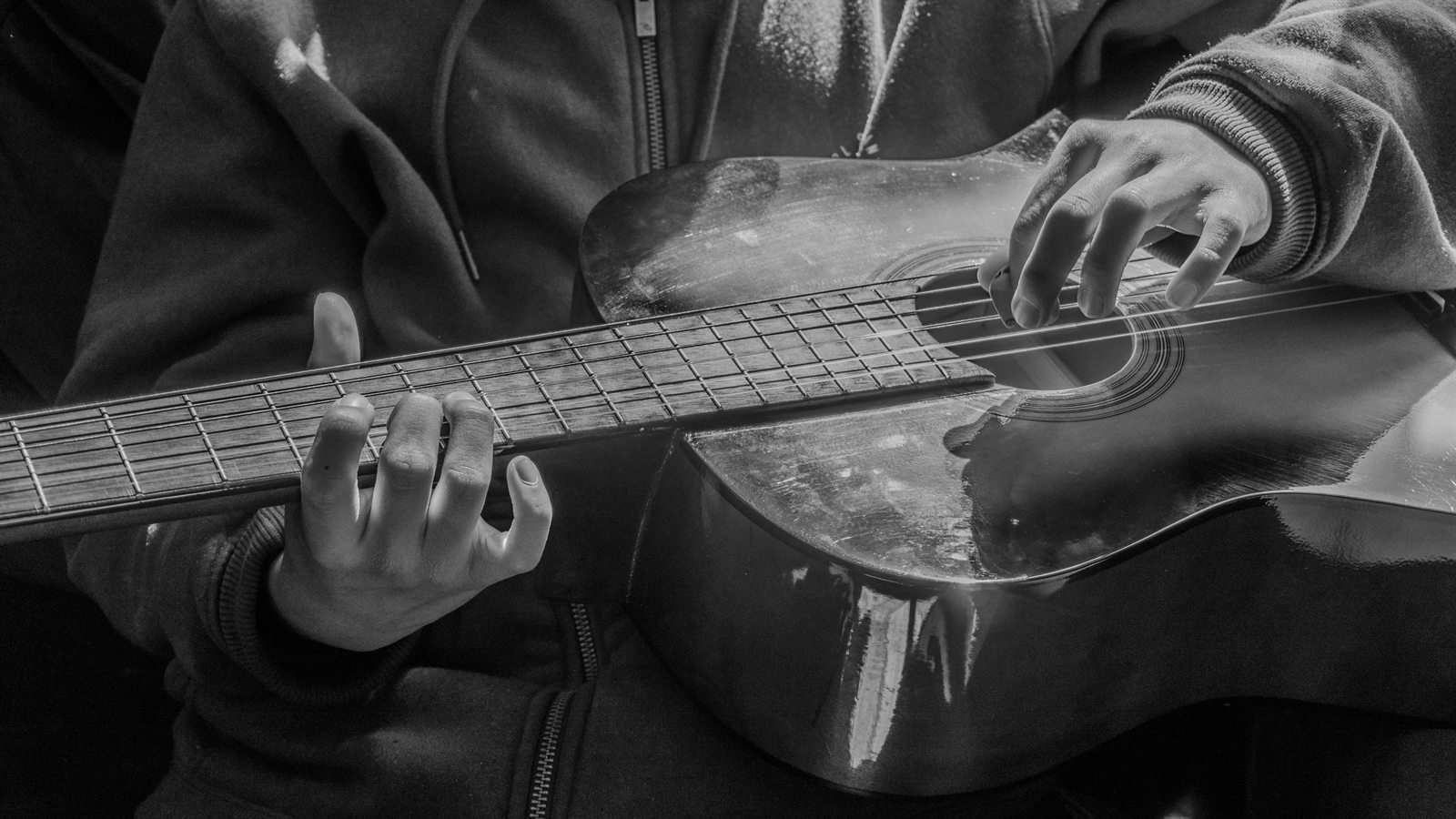 Manos tocando una guitarra acústica sobre una sudadera.
